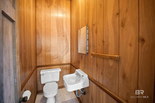 half bathroom with wooden walls, toilet, and a sink