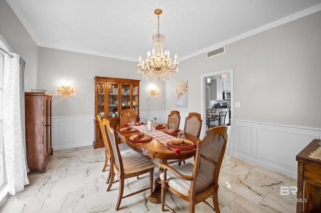 dining room with an inviting chandelier, wainscoting, marble finish floor, visible vents, and ornamental molding