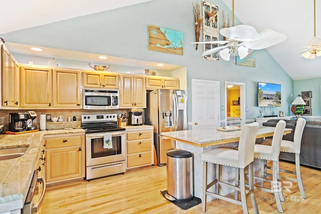 kitchen with light wood finished floors, appliances with stainless steel finishes, a ceiling fan, open floor plan, and light brown cabinets
