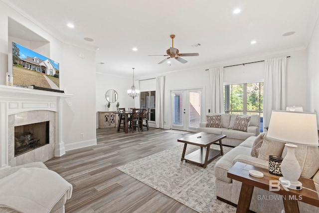 living room with hardwood / wood-style floors, french doors, ceiling fan with notable chandelier, ornamental molding, and a premium fireplace