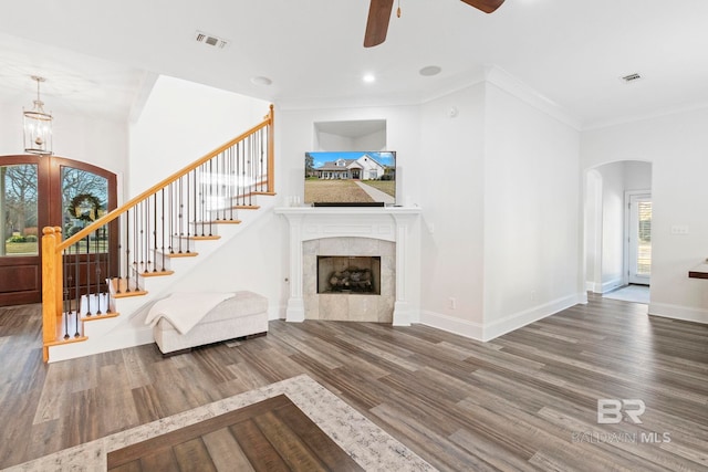 unfurnished living room featuring ceiling fan, wood-type flooring, ornamental molding, and a tiled fireplace