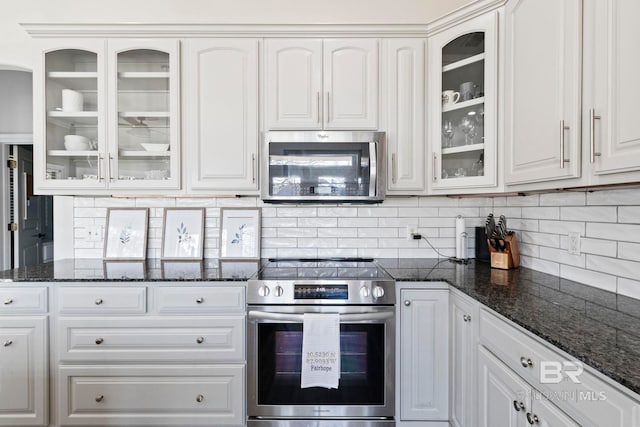 kitchen featuring white cabinets, backsplash, stainless steel appliances, and dark stone counters