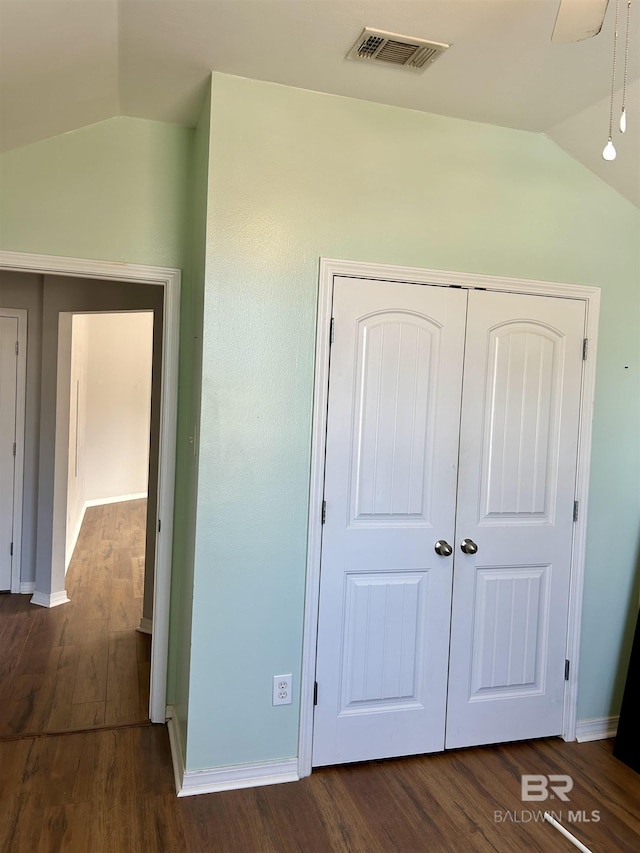 unfurnished bedroom with lofted ceiling, a closet, visible vents, and dark wood-style flooring