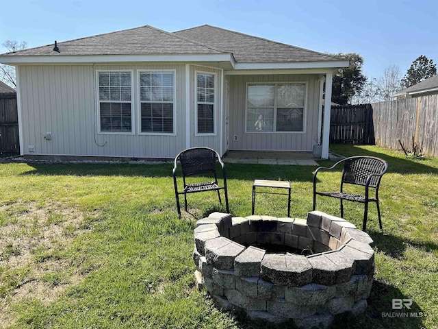 back of house featuring a yard, an outdoor fire pit, a fenced backyard, and roof with shingles