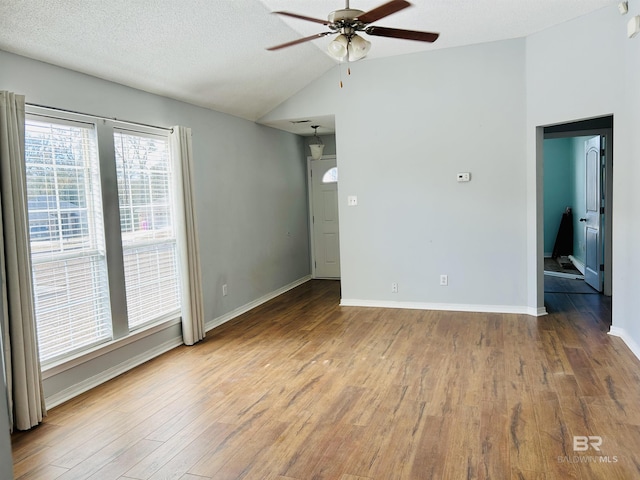 empty room with a ceiling fan, wood finished floors, baseboards, lofted ceiling, and a textured ceiling