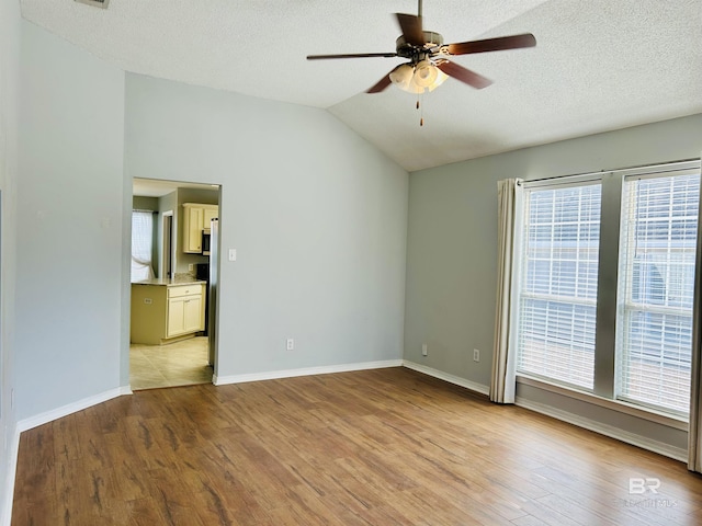 unfurnished room with vaulted ceiling, plenty of natural light, a ceiling fan, and light wood finished floors