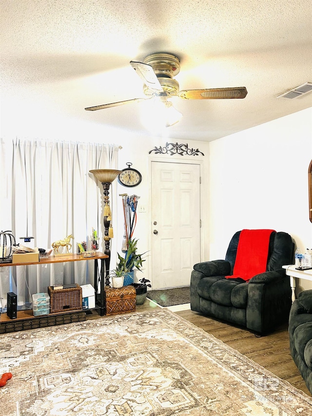 living area with a ceiling fan, visible vents, a textured ceiling, and wood finished floors