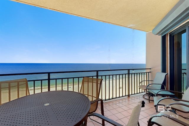 balcony with outdoor dining area, a view of the beach, and a water view