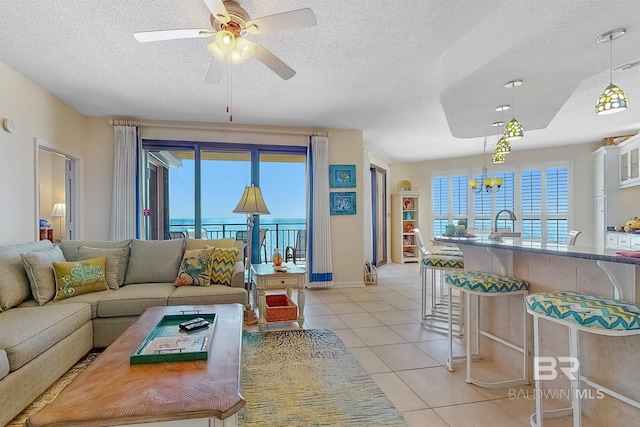 living area featuring a textured ceiling, light tile patterned flooring, and ceiling fan with notable chandelier