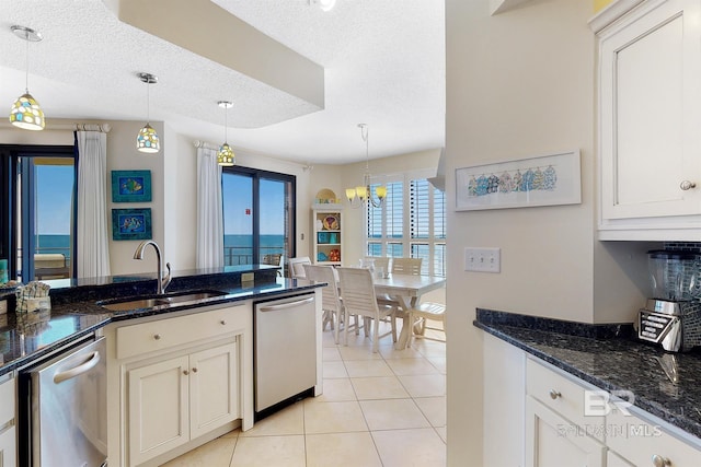 kitchen with dark stone countertops, light tile patterned floors, a sink, dishwasher, and decorative light fixtures