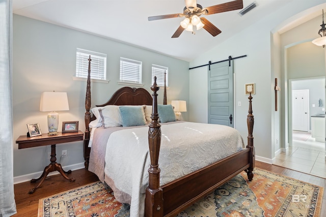 bedroom featuring ceiling fan, a barn door, light wood-type flooring, and vaulted ceiling