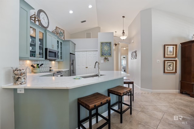 kitchen with pendant lighting, lofted ceiling, blue cabinetry, appliances with stainless steel finishes, and kitchen peninsula