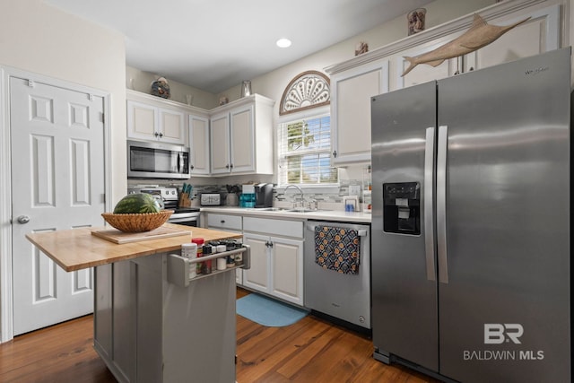 kitchen with white cabinets, wood counters, appliances with stainless steel finishes, a center island, and a sink