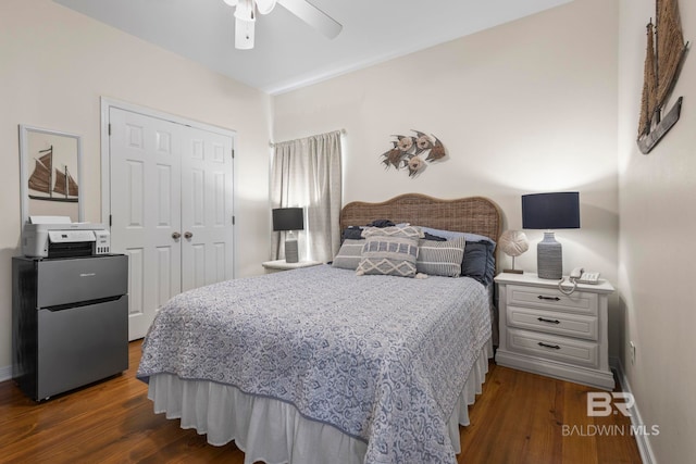 bedroom featuring a ceiling fan, baseboards, a closet, freestanding refrigerator, and dark wood-style floors