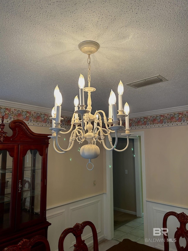 unfurnished dining area with crown molding, wainscoting, visible vents, and a textured ceiling