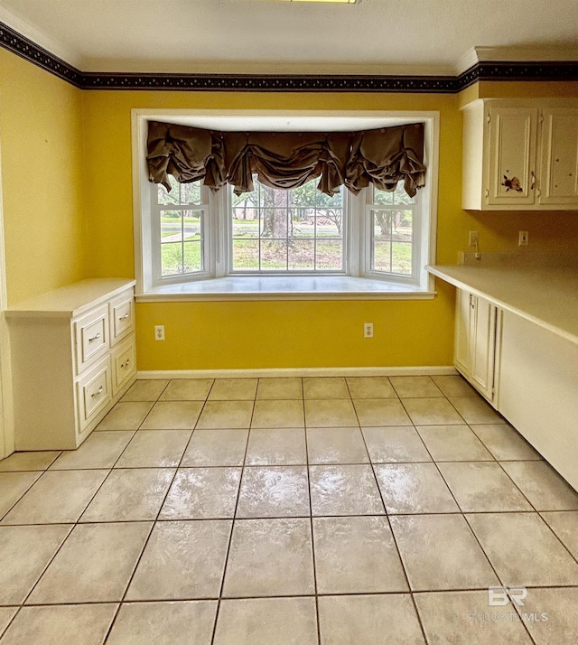 unfurnished dining area with baseboards, light tile patterned flooring, and crown molding