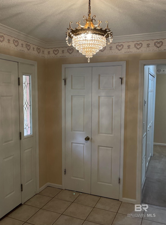 foyer entrance with ornamental molding, a textured ceiling, light tile patterned flooring, baseboards, and a chandelier