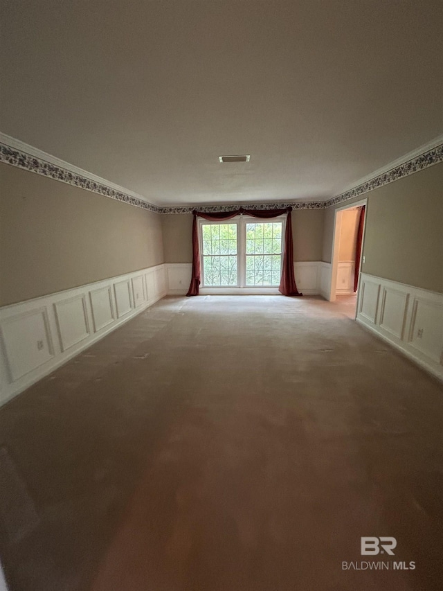 empty room with a wainscoted wall, carpet floors, visible vents, and a decorative wall