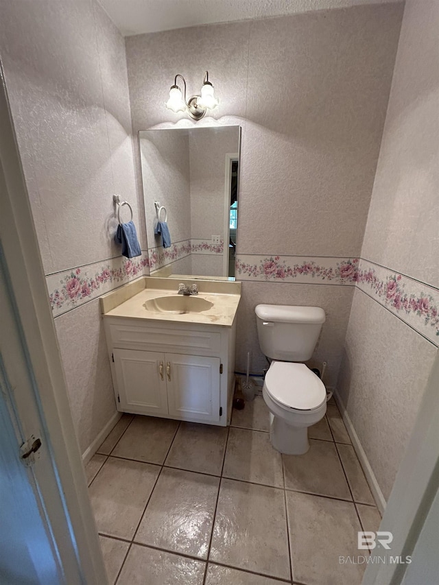 half bathroom featuring vanity, baseboards, tile patterned flooring, toilet, and a textured wall