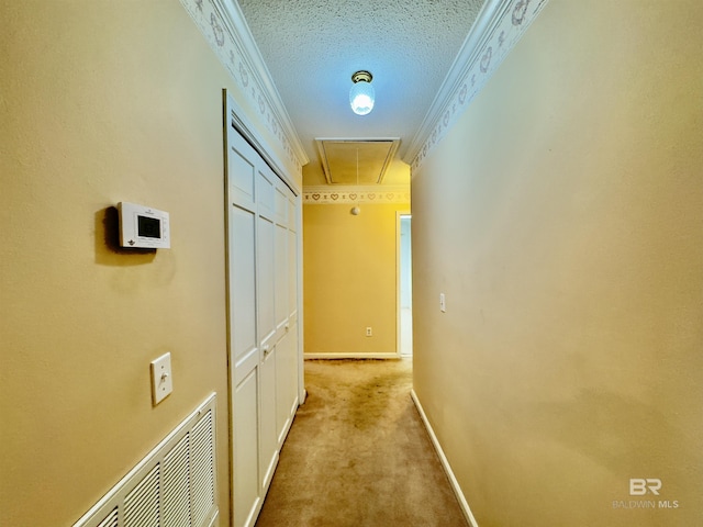 hallway featuring visible vents, light colored carpet, attic access, ornamental molding, and a textured ceiling