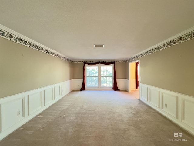 unfurnished room with visible vents, light colored carpet, a wainscoted wall, and crown molding