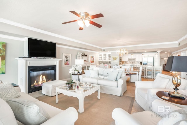 living room with ornamental molding, a glass covered fireplace, ceiling fan with notable chandelier, and light tile patterned floors