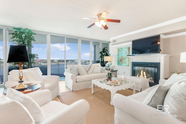 living area featuring floor to ceiling windows, visible vents, a ceiling fan, a glass covered fireplace, and ornamental molding