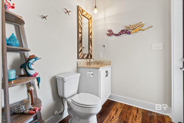half bath with baseboards, wood finished floors, toilet, and vanity