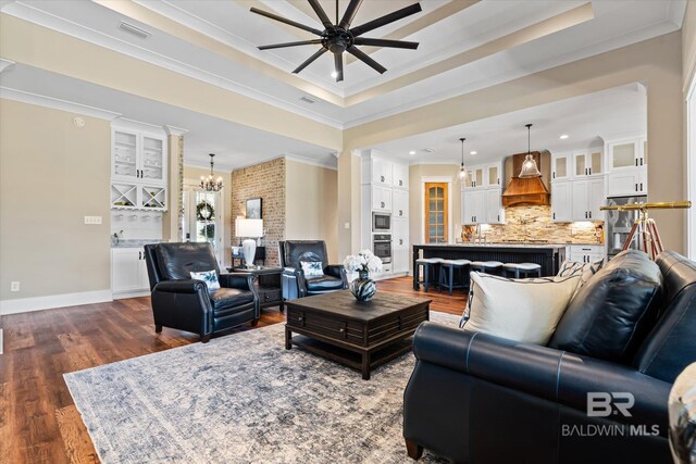 living area featuring crown molding, ceiling fan with notable chandelier, dark wood finished floors, a raised ceiling, and visible vents