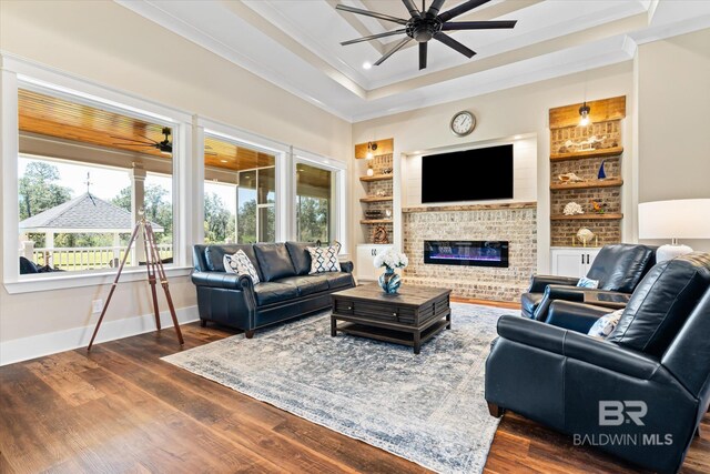 living room featuring built in features, crown molding, a raised ceiling, and a ceiling fan
