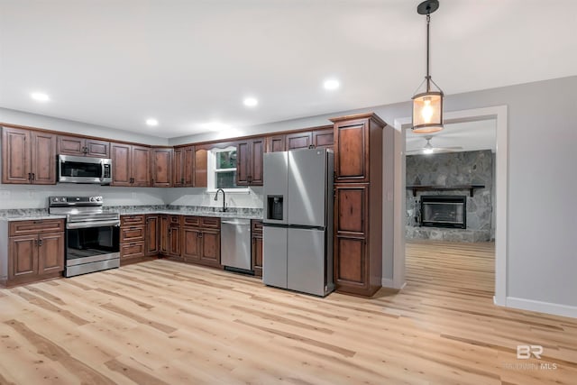 kitchen featuring light wood-type flooring, light stone counters, hanging light fixtures, a fireplace, and appliances with stainless steel finishes