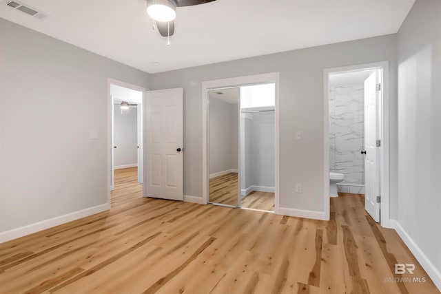 unfurnished bedroom featuring connected bathroom, a closet, ceiling fan, light hardwood / wood-style flooring, and a walk in closet