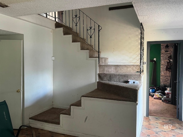 stairway with carpet floors and a textured ceiling