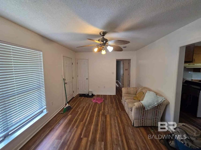 living area with a ceiling fan, wood finished floors, a textured ceiling, and baseboards