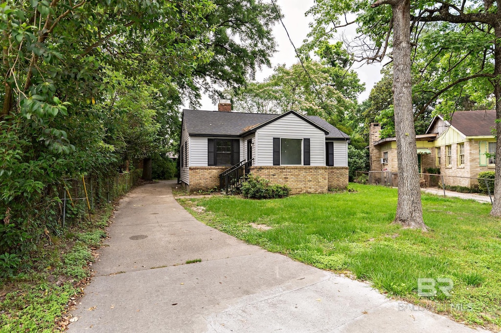 bungalow-style home featuring fence, a chimney, brick siding, a front lawn, and driveway
