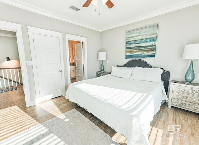 bedroom with ceiling fan, wood finished floors, visible vents, ornamental molding, and ensuite bath