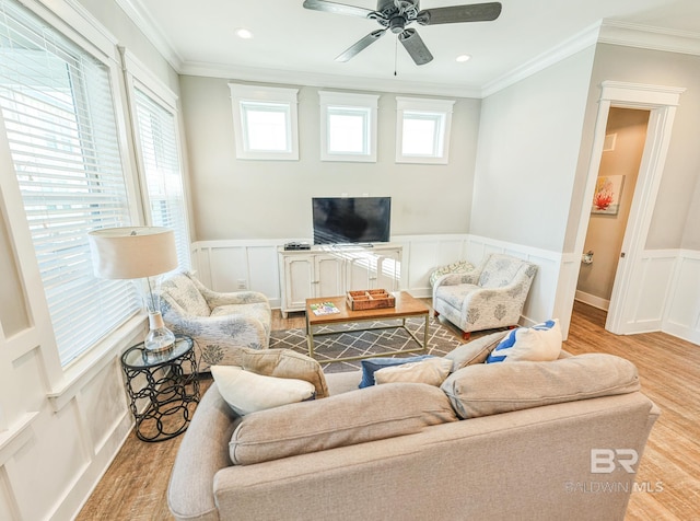 living area featuring a wainscoted wall, ceiling fan, light wood-style floors, and crown molding