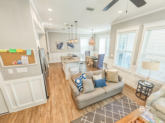 living room featuring light wood-style floors, visible vents, crown molding, and a decorative wall