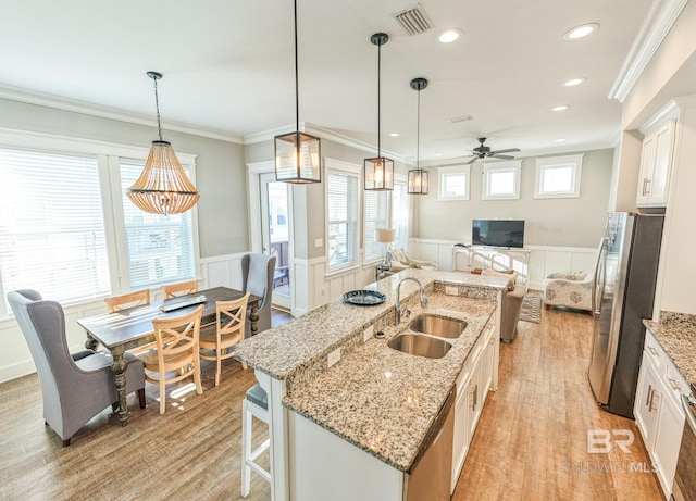 kitchen with a wainscoted wall, stainless steel appliances, a sink, visible vents, and open floor plan