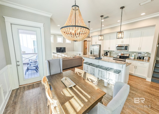 dining area featuring a wainscoted wall, visible vents, crown molding, and a decorative wall