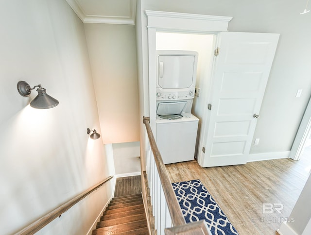 clothes washing area with stacked washer and dryer, crown molding, baseboards, and wood finished floors