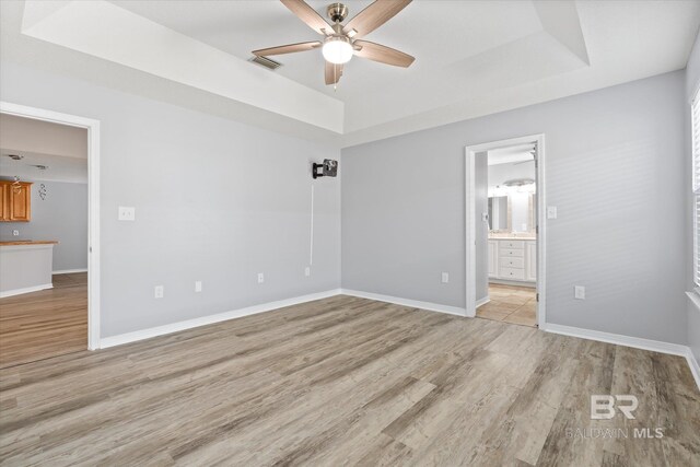 26715 Terry Cove Dr, Orange Beach, AL 36561 - unfurnished bedroom featuring a tray ceiling, light wood-style flooring, baseboards, and ensuite bathroom