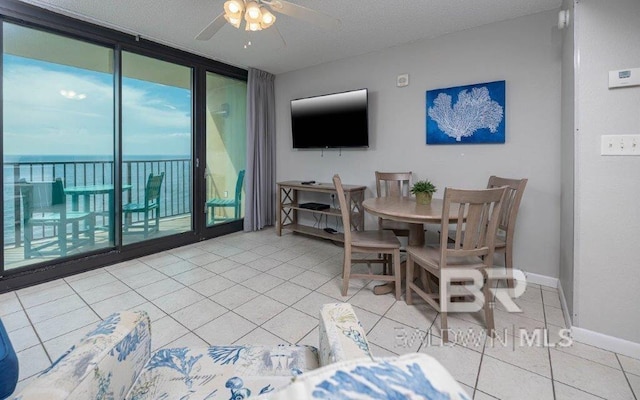 tiled dining room with ceiling fan, a water view, and a textured ceiling