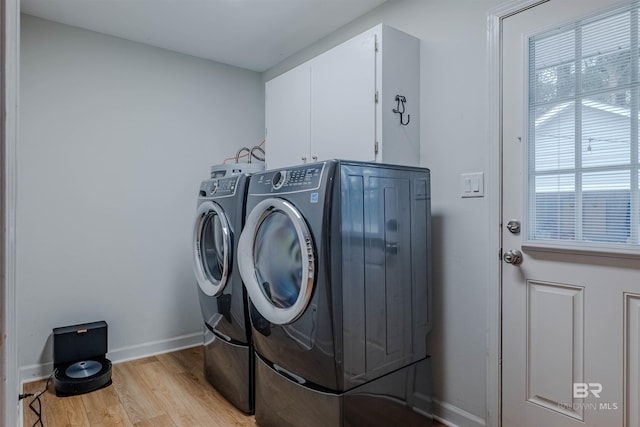 clothes washing area with separate washer and dryer, light hardwood / wood-style flooring, and cabinets