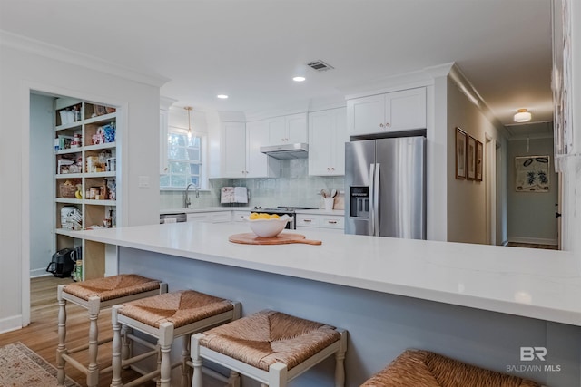 kitchen with a breakfast bar area, white cabinetry, hanging light fixtures, stainless steel appliances, and light hardwood / wood-style floors