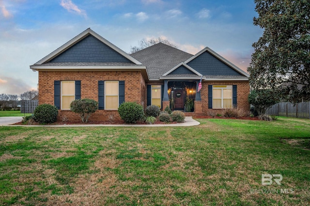 craftsman house with a yard, a shingled roof, fence, and brick siding