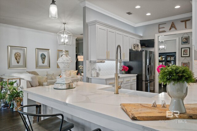 kitchen with a breakfast bar area, a sink, white cabinets, backsplash, and crown molding