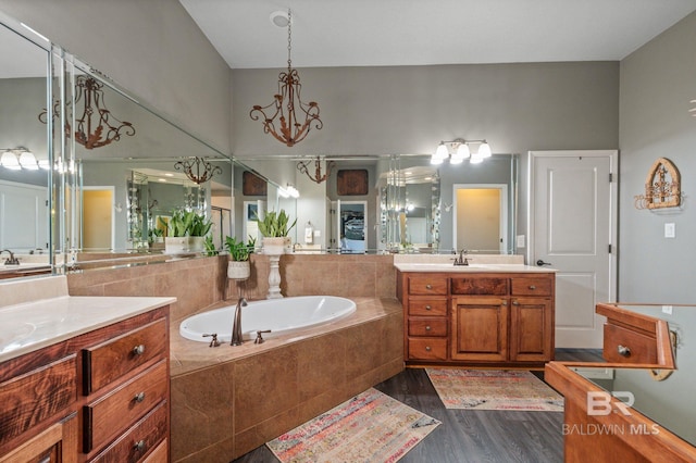 full bathroom featuring a chandelier, a garden tub, wood finished floors, two vanities, and a sink