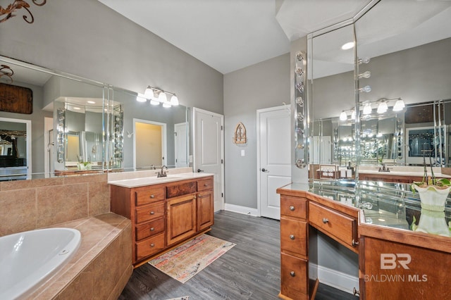 full bath with baseboards, lofted ceiling, wood finished floors, vanity, and a bath