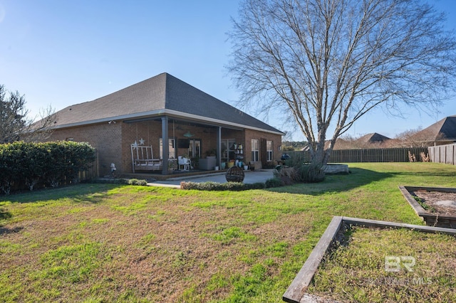 rear view of house featuring brick siding, a yard, a vegetable garden, a patio, and fence